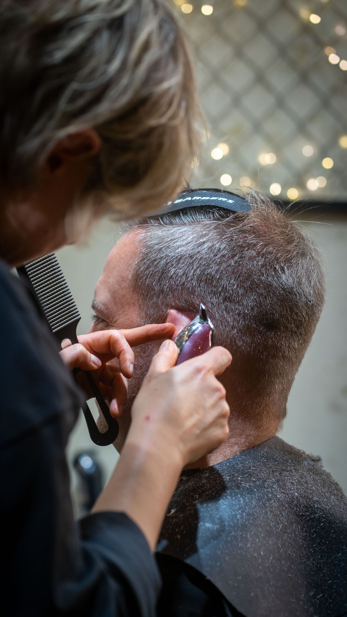 Stylistin arbeitet mit Trimmer und Kamm die Konturen eines Herrenhaarschnitts aus